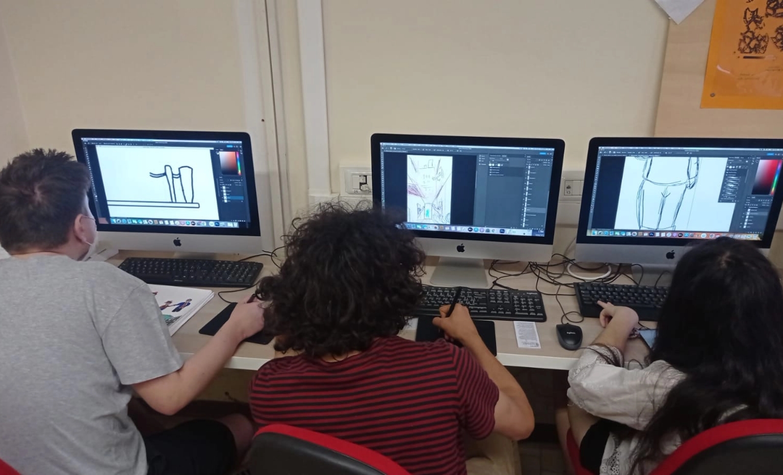 Tre ragazzi al lavoro con computer e tavoletta grafica sui disegni del progetto.
